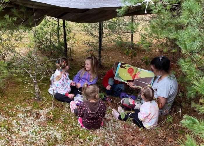 Five children sitting outdoors and listening to an adult tell a story