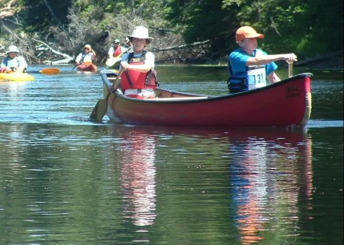 Two people paddling in a canoe on a lake with other people in canoes in the background