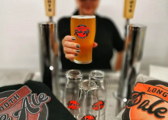 Person holding a pint of beer up in towards the camera with two beer taps on either side