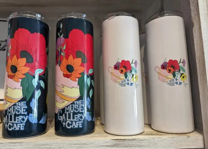 Shelf with four reusable drinking cylinders, two with flowers and name of venue, two white with basket of flowers