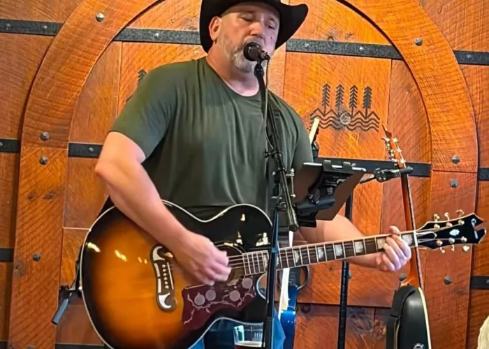 Craig McEachern singing onstage holding guitar, wooden wall background, event details